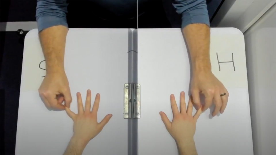 Two hands are spread on a table, a person opposite is holding the little finger tips on each hand